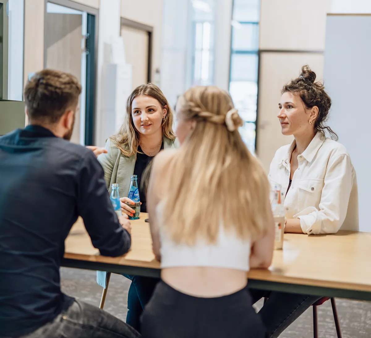Four people sitting at a table having a casual conversation in an office setting.