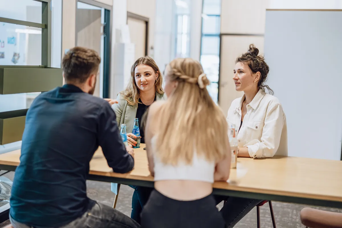 Four people sitting at a table having a casual conversation in an office setting.