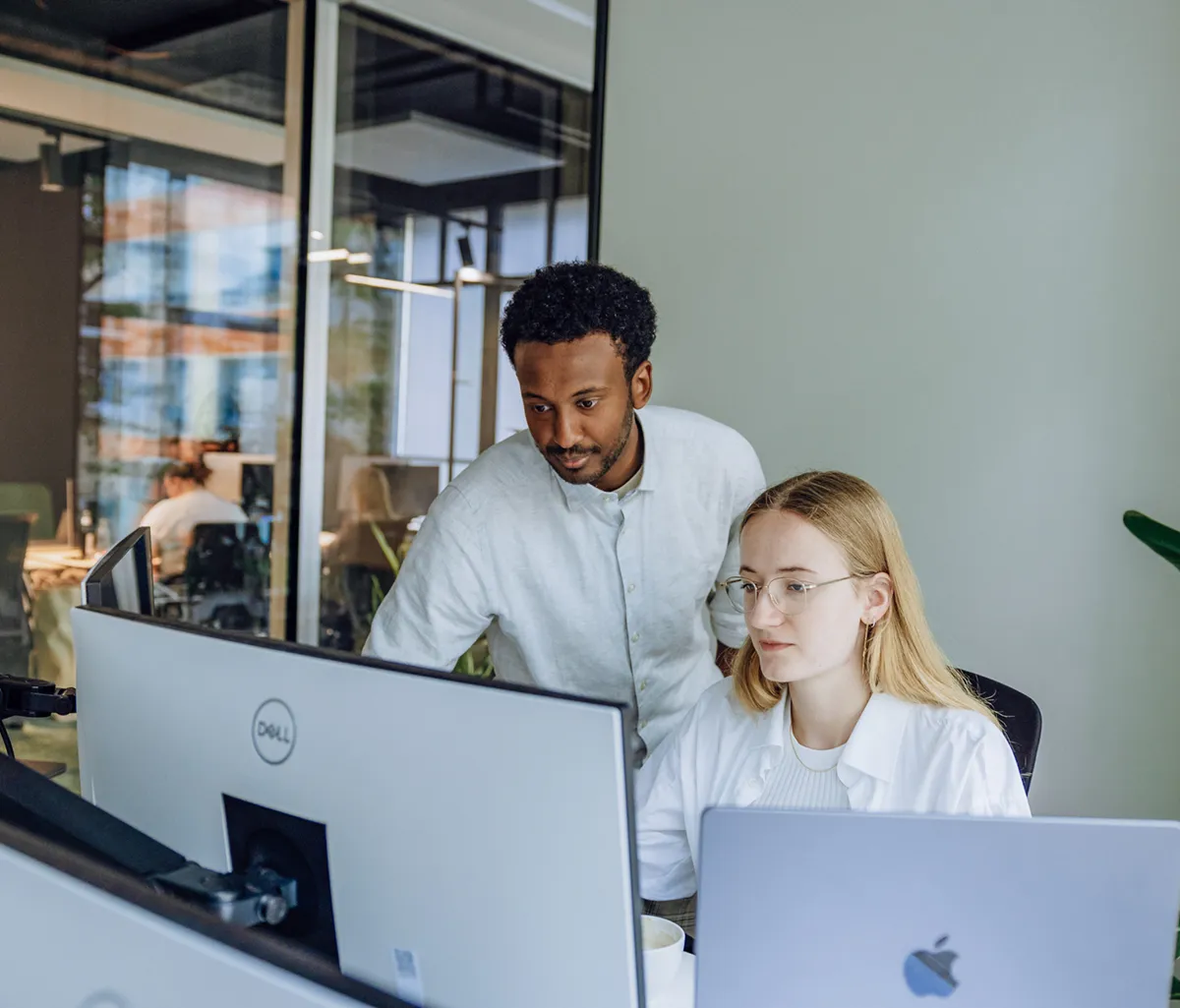 Two colleagues collaborating at a desk with computers in a modern office setting.
