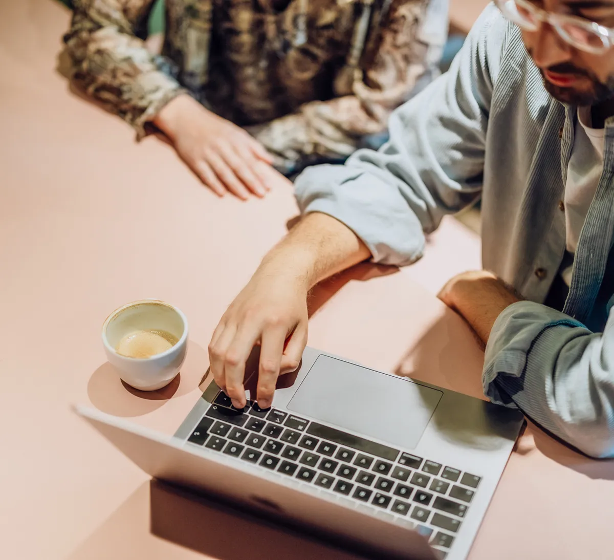 Two people sitting at a table with a laptop and a cup of coffee, focusing on the screen.