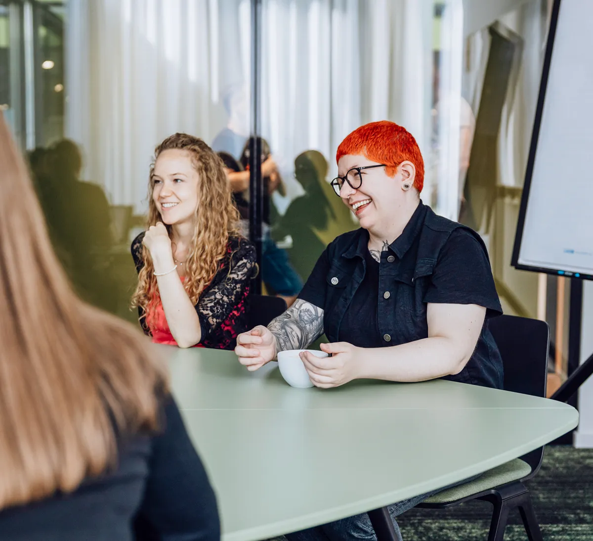 Two people sitting at a table, smiling and engaged in conversation, with a flipchart in the background.