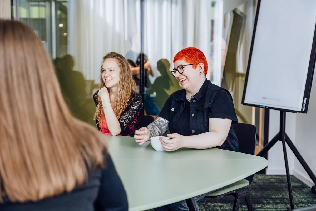 Two people sitting at a table, smiling and engaged in conversation, with a flipchart in the background.